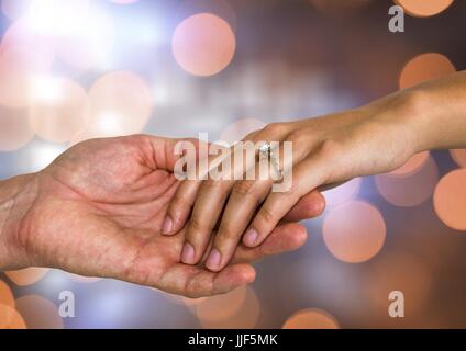 Digital composite of Couple Hands holding engagement wedding ring with sparkling light bokeh background Stock Photo