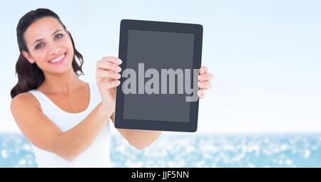 Digital composite of Smiling woman holding out tablet against blurry water on sunny day Stock Photo