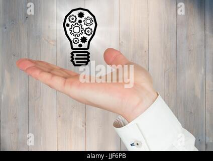 Digital composite of Hand with cogs in lightbulb graphic and flare against grey wood panel Stock Photo