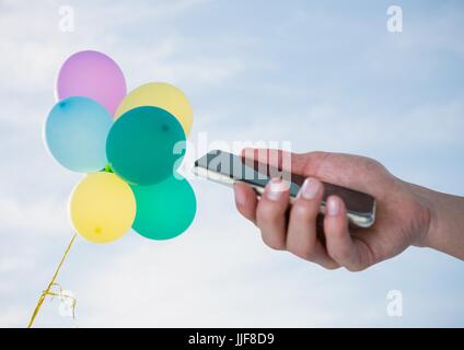 Digital composite of Hand with phone against sky and balloons Stock Photo