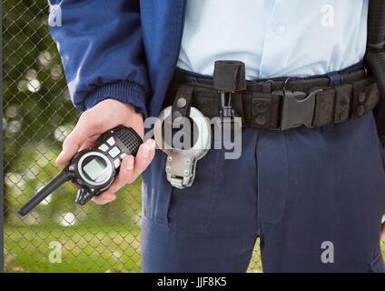 Digital composite of security guard with walkie-talkie on his hand and cuffs on the belt in front of the fence Stock Photo