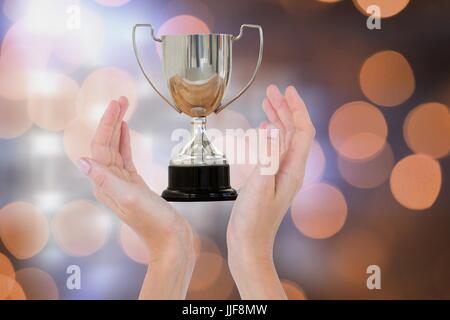 Digital composite of Hands holding trophy against orange glowing background Stock Photo