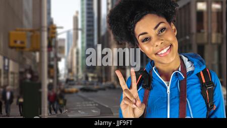 Digital composite of Smiling hipster carrying backpack with camera gesturing peace sign standing in city Stock Photo