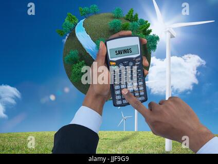 Digital composite of Digital composite image of hands using calculator with planet earth and windmills on grassy field ag Stock Photo