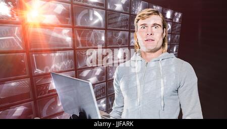 Digital composite of Hacker holding laptop standing by digital screen Stock Photo