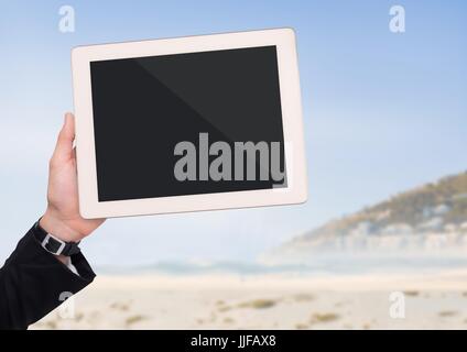 Digital composite of Hand with tablet against blurry beach Stock Photo