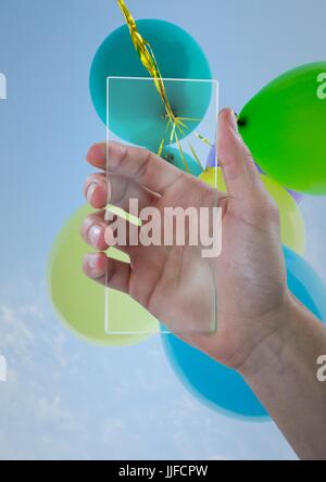 Digital composite of Hand with glass device against sky and balloons Stock Photo