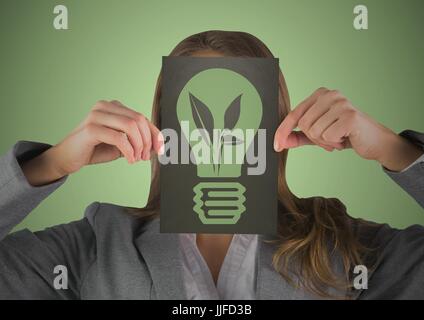 Digital composite of Business woman with black card over face showing green lightbulb graphic against green background Stock Photo