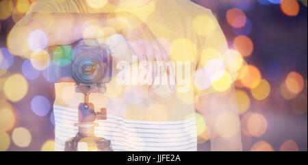 Mid section of photographer standing with camera on tripod against composite image of brown parquet Stock Photo