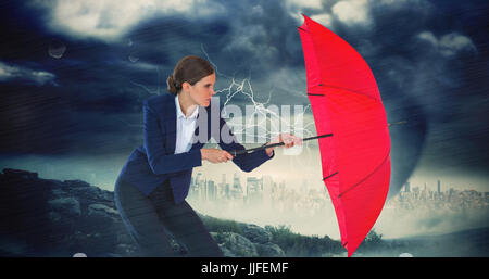 Businesswoman holding red umbrella against stormy sky with tornado over cityscape Stock Photo