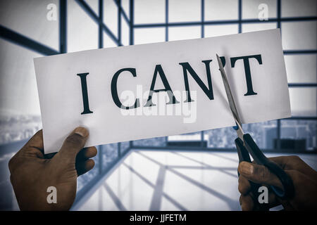 Conceptual image of businessman cutting paper that reads we cant  against room with large windows showing city Stock Photo