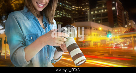 Portrait of young female photographer holding camera against illuminated roads by building in city Stock Photo