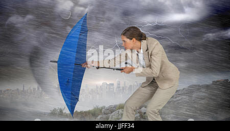 Full length of businesswoman defending with blue umbrella  against stormy sky with tornado over cityscape Stock Photo