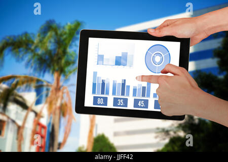 Hands touching digital tablet against white background against tree by glass building Stock Photo