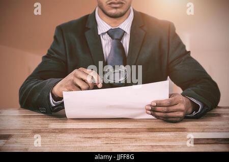 Businessman looking at document through magnifying glass against bright room with two closed doors Stock Photo