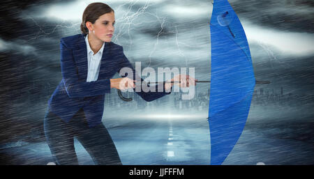 Confident businesswoman defending with blue umbrella against stormy sky with tornado over road Stock Photo