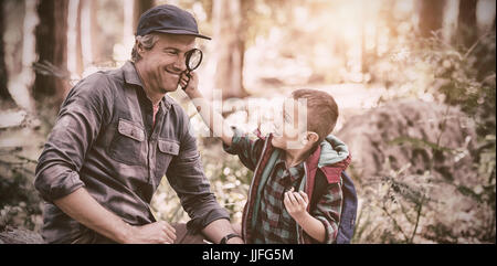 Curious little boy showing magnifying glass to father while hiking in forest Stock Photo