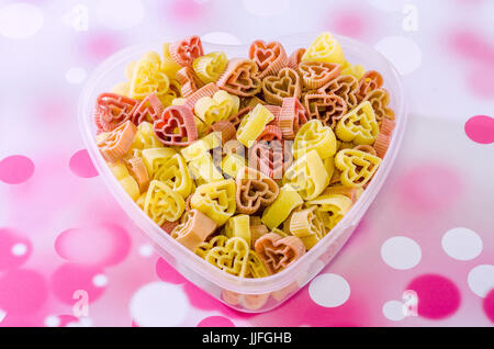 Transparent heart shape vase (bowl) filled with colored (red) heart shape jellies, bokeh background, close up Stock Photo