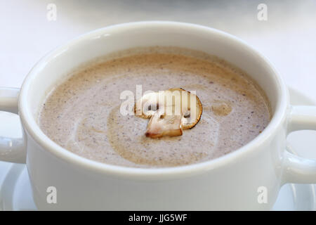 Portion of champignon mushroom cream soup in white porcelain tureen pot on the table, close up, high key, high angle view Stock Photo