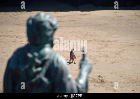 Statue of St Crannog looking down onto holidaymakers on Llangrannog beach, Ceredigion, Wales Stock Photo