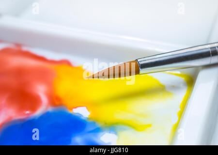 Watercolor paint brush on a white palette with the fluid paint merging together, in an artist's studio Stock Photo
