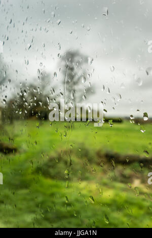 Raindrops on a glass. Rain on a window with garden landscape as background. Feeling of sadness. France, Europe Stock Photo