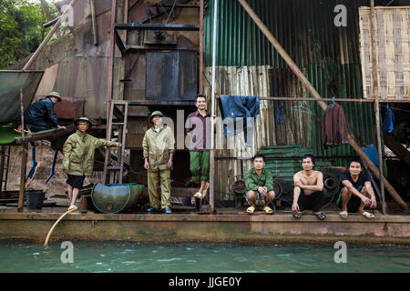 Vietnamese and Lao men stand on the deck of a mechanical gold dredge floating on the Nam Ou River, Laos. Stock Photo