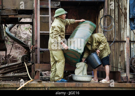 Vietnamese men empty out concentrate from the sluice box into a bag for later processing on the deck of a mechanical gold dredge floating on the Nam Ou River, Laos. Stock Photo