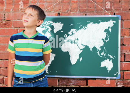 Meditative boy near chalkboard with drawing Earth map in the improvised outdoor class Stock Photo