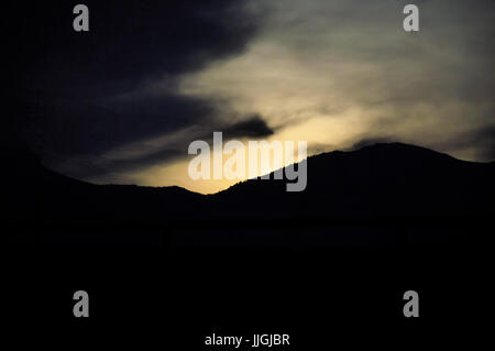 Sunrise coming over a mountain through clouds. Stock Photo