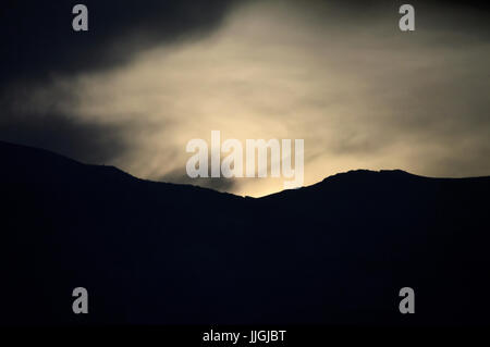 Sunrise coming over a mountain through clouds. Stock Photo
