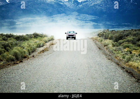 A ford pickup truck driving down a gravel road with dust billowing out behind it. Stock Photo