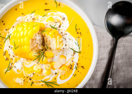 Vegan cuisine. Traditional autumn corn soup. Served with corn cobs, greens, cream. On a white marble table. Close top view Stock Photo