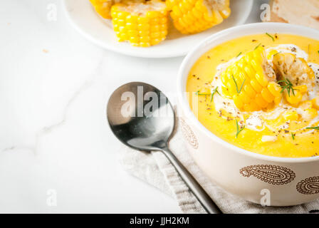 Vegan cuisine. Traditional autumn corn soup. Served with corn cobs, greens, cream. On a white marble table. Copy space Stock Photo