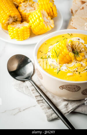 Vegan cuisine. Traditional autumn corn soup. Served with corn cobs, greens, cream. On a white marble table. Copy space Stock Photo