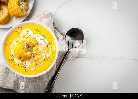 Vegan cuisine. Traditional autumn corn soup. Served with corn cobs, greens, cream. On a white marble table. Copy space top view Stock Photo