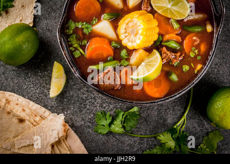 Autumnal vegetable stew. Mexican traditional vegetable soup Mole de olla with meat, potatoes, carrots, beans, corn and lime. Copy space top view Stock Photo