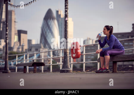 A woman resting after a run alongside the River Thames in London. Stock Photo
