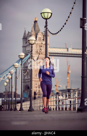 A woman running alongside the River Thames with Tower Bridge in the background. Stock Photo