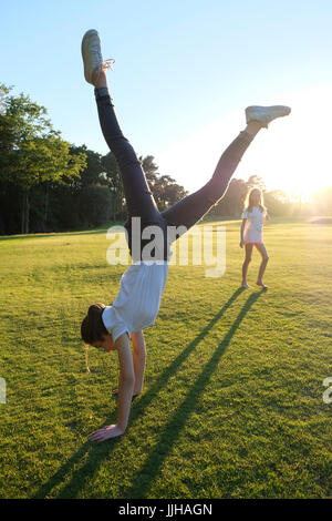 A teenage girl doing a handstand watched by her sister. Stock Photo