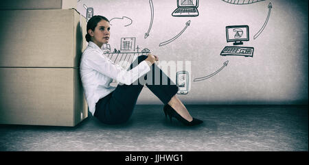 Businesswoman leaning on cardboard boxes against white background against grey room Stock Photo