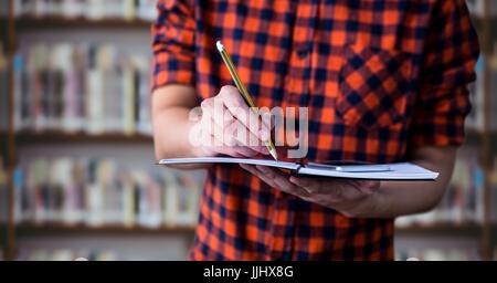 College student mid section with notebook against blurry bookshelf Stock Photo