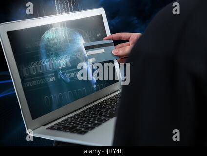 Hacker holding a credit card and using a laptop with 3D digital face on screen Stock Photo