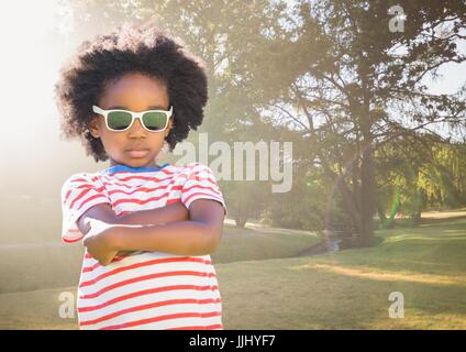 Boy in sunglasses arms folded against blurry park with flare Stock Photo