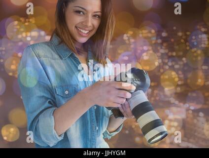 photographer woman smiling with camera on hands in the balcony. city nights lights and flares Stock Photo