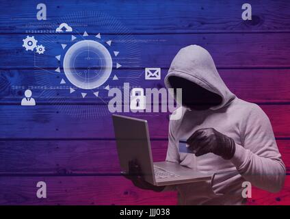 Hacker with hood holding a credit card and using a laptop in frond of wood background with digital i Stock Photo