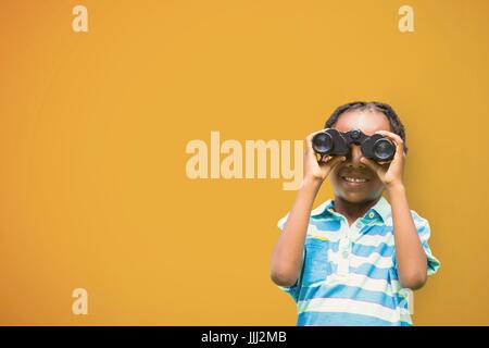 Happy boy looking through binoculars against yellow background Stock Photo