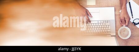 Overhead of hands typing on laptop and holding coffee with blurry orange transition Stock Photo