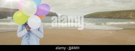 Woman mid section with balloons on beach with flare 3d Stock Photo