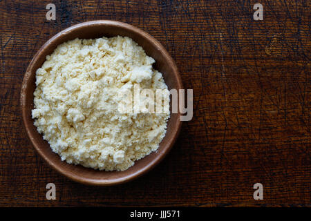 Corn flour in dark wooden bowl isolated on dark brown wood from above. Stock Photo